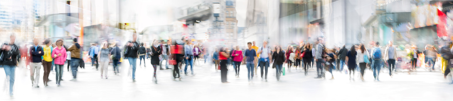 A blurred image of crowd of people walking through a city.