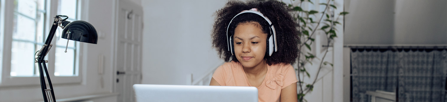 Photo of a young black girl attending virtual school at her home.