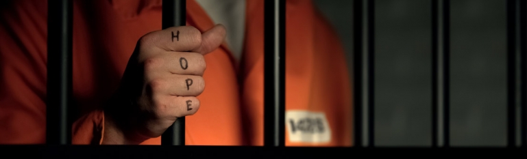 A youth holding prison bars. The word HOPE is tattooed on his hand