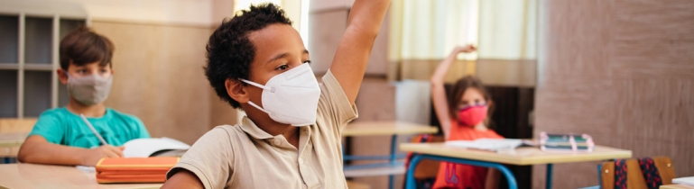 A little boy in a classroom wearing a medical mask to protect herself from COVID
