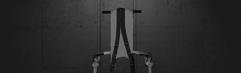 An image of a jail restraint chair in a dark room.