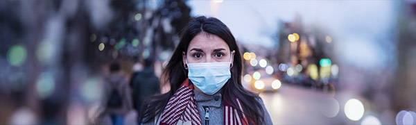 Photo of a lone woman in the street wearing a medical mask to prevent spread of germs.