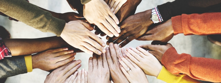 Photo of people of different races hands together in a circle. 