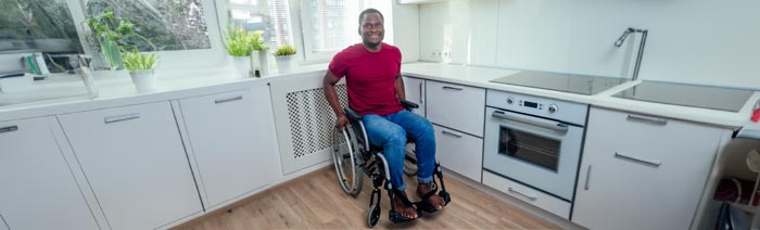A black man in a wheel chair in his kitchen and looking at camera.