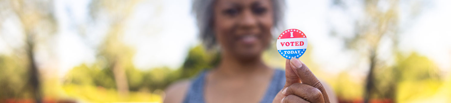 A black woman holding up a sticker saying she voted.