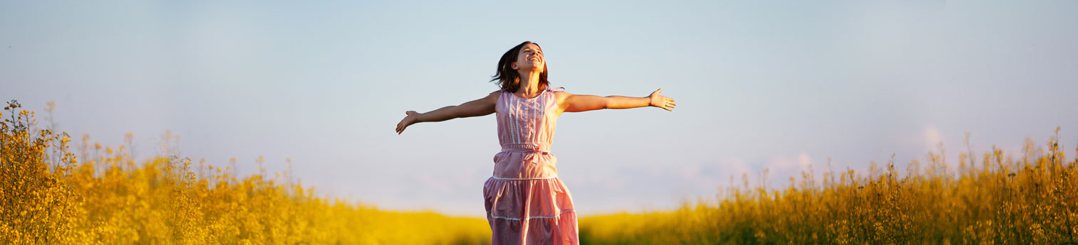 A happy woman smiling with her arms spread. She is outside on a beautiful day in a large golden field of tall grass.