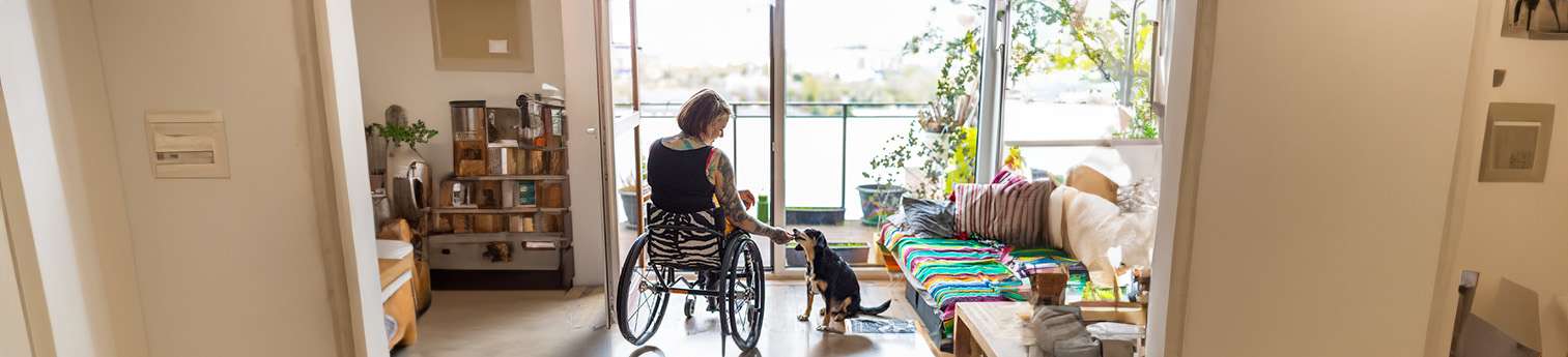 A woman in a wheelchair feeding her dog inside of her home.