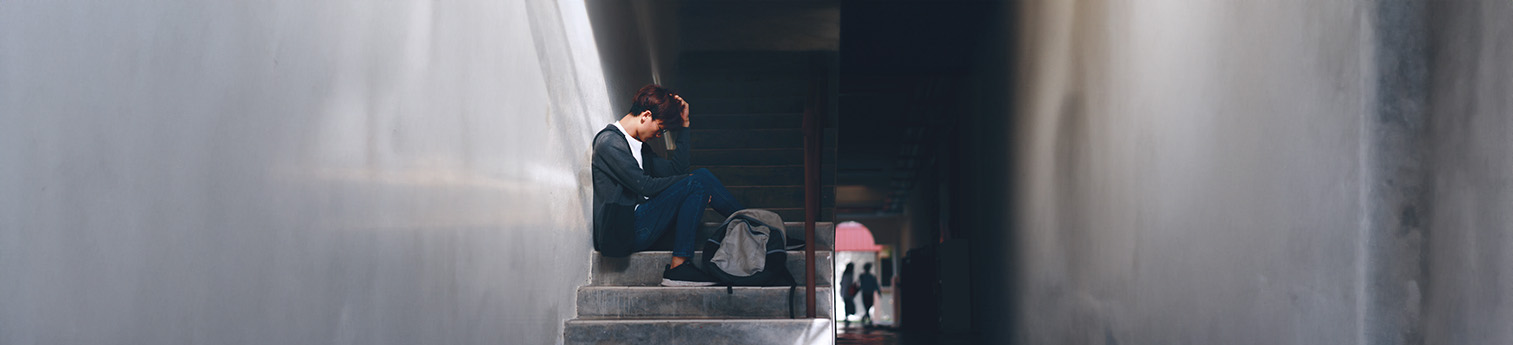 A young Asian male, sitting on stairs with his head down. 