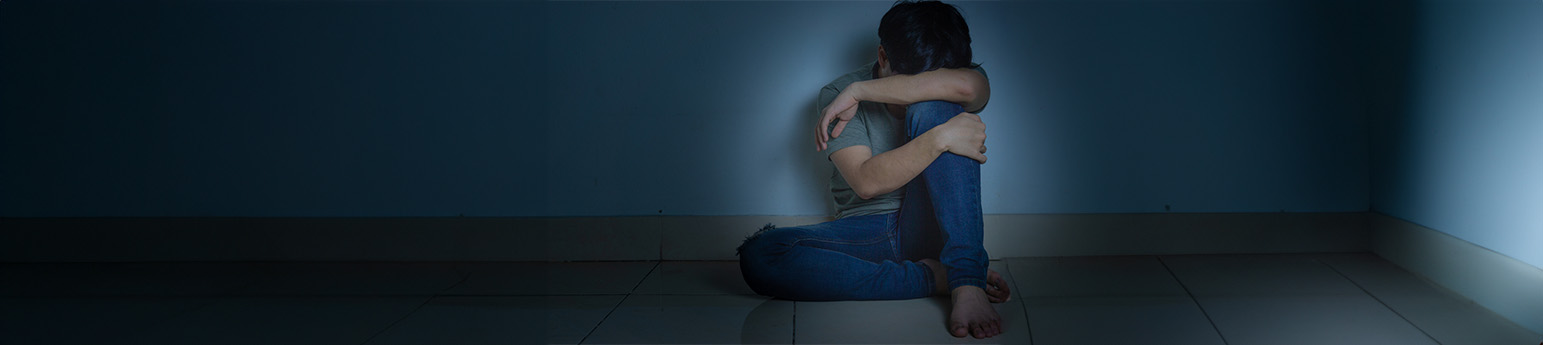 A male hugging his knees in a dark room.