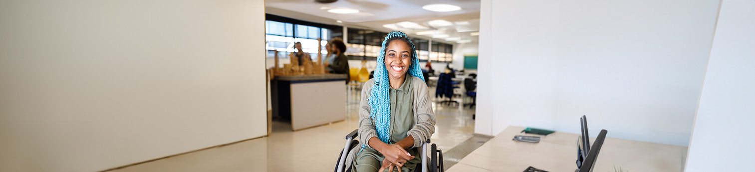 A black woman in a wheelchair with light blue braids, smiling.
