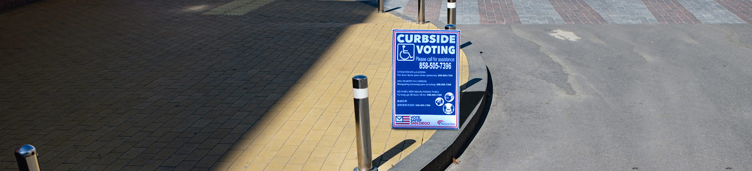 A curbside voting sign at the edge of a sidewalk curb.