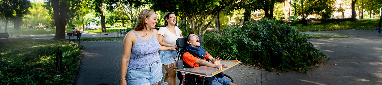 Family of Two Latina women and a Latino male in a wheelchair walking and talking on the public park.