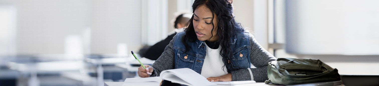 A black female student doing her homework in a school classroom.