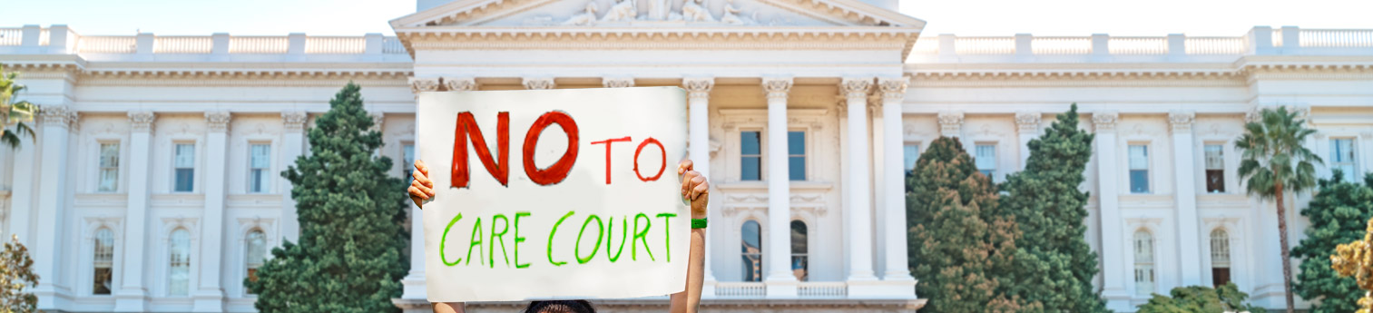 A protestor in front of the California State Capitol holding up a sign that says - NO TO CARE COURT