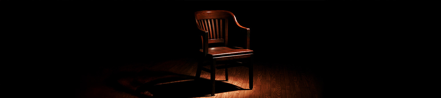 A spotlight on singular wooden chair on wooden floor.