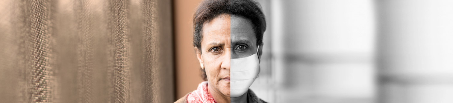 Photo of a hispanic woman. Half of her face is covered with a Covid medical mask to represent separation.