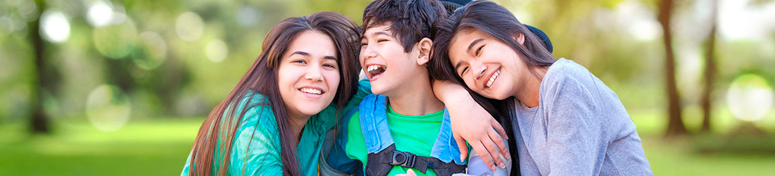 Two sisters hugging their brother who has a disability and is in a wheelchair.