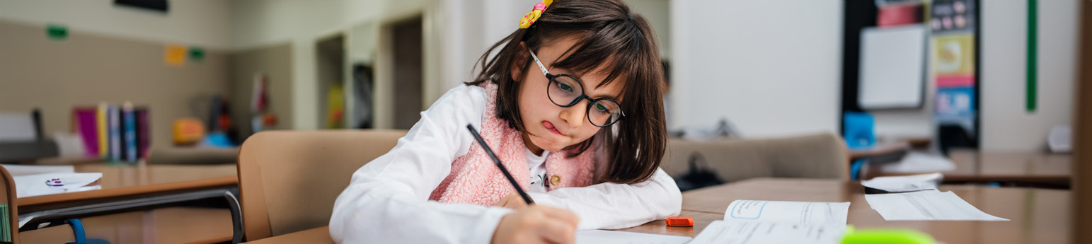 A young girl with a disability at her desk doing schoolwork in a classroom.