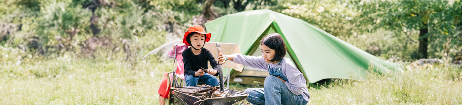 Hai đứa trẻ châu Á bên đống lửa trại. Họ có một cái lều đằng sau họ.