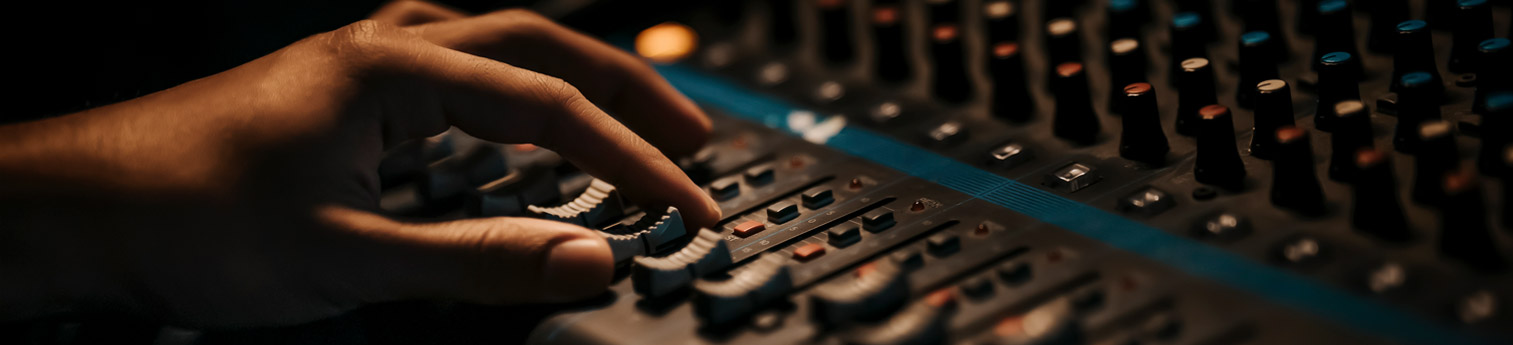 Close up of a hand make adjustments on a sound editing control board.