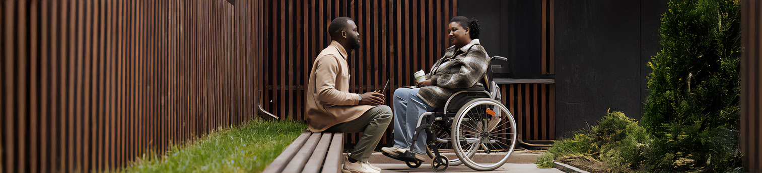 Side view shot of a Black woman in a wheelchair talking to a Black male colleague outdoors in city park.