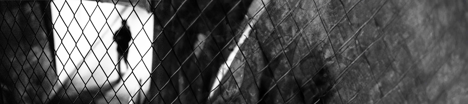 A shadow of a person behind barbed wire.