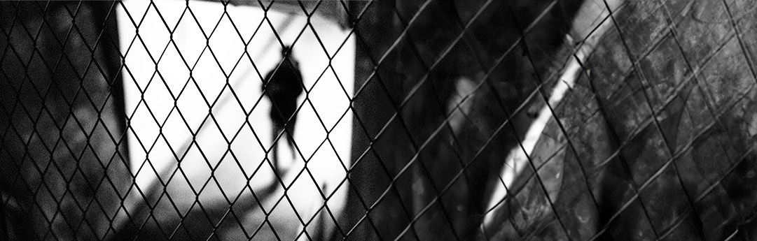 A shadow of a person behind barbed wire.