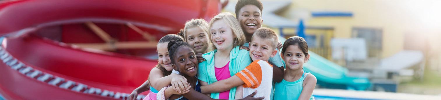 A group or children at a park laughing and hugging each other. They all have different disabilities and are of different disabilities.