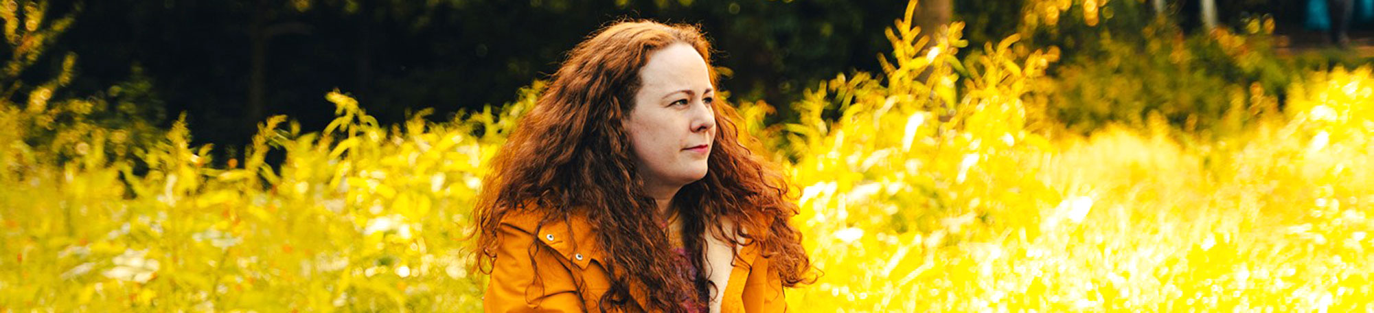 A still photo from Alice McCullough's film 'Earth to Alice'. She is sitting on a brick bridge with lush, tall, green foliage surrounding her.