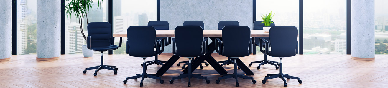 Photo of an empty board room. There is a large table in the room surround by chairs.