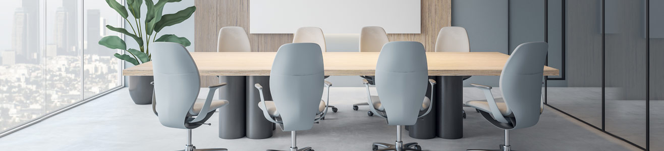 A picture of a board room office filled with office chairs surrounding a long desk used for group meetings.