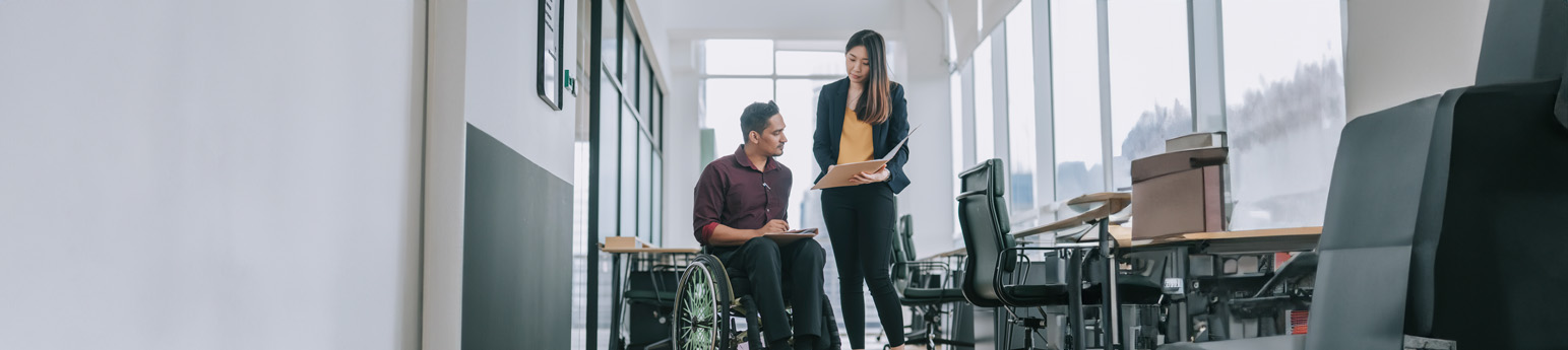 I man in a wheelchair at the office talking to a woman standing next to him