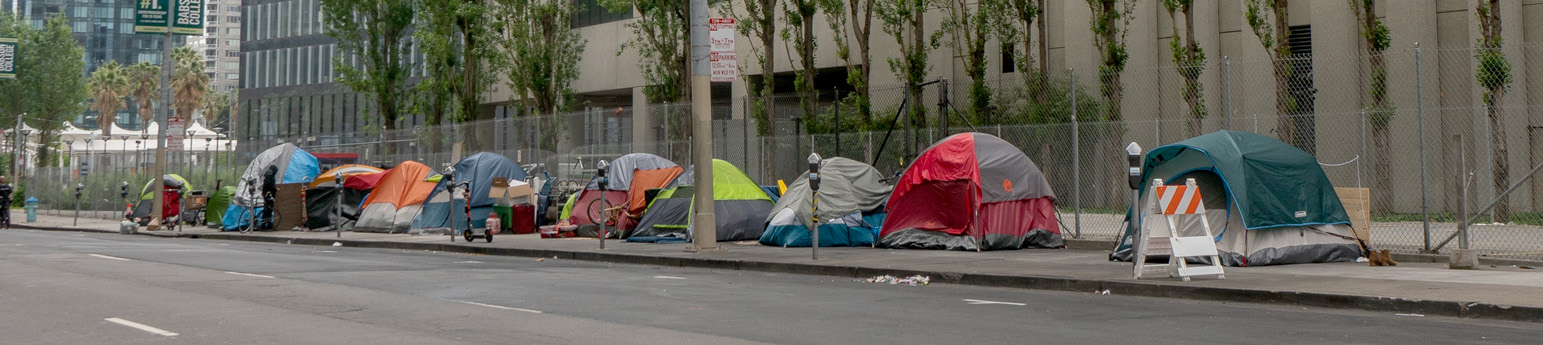 A city street with several tents on the sidewalk that homeless people are using.