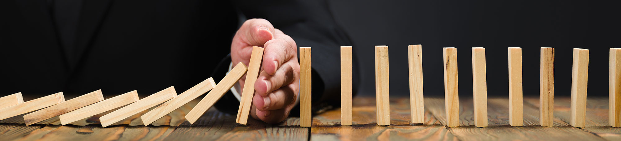 The hand of a man in a suit preventing a row of dominos from crashing.