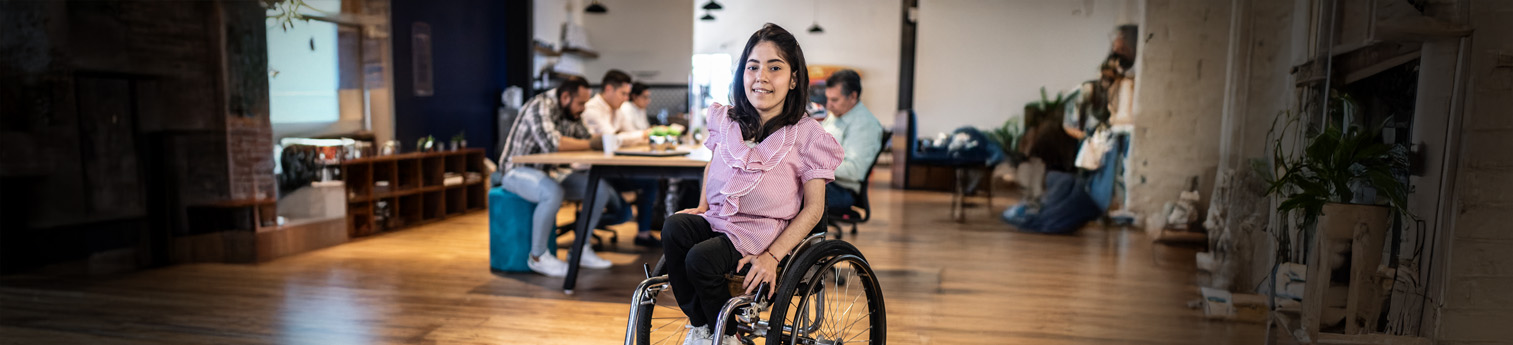 A young disabled woman in a wheelchair in a large office room.