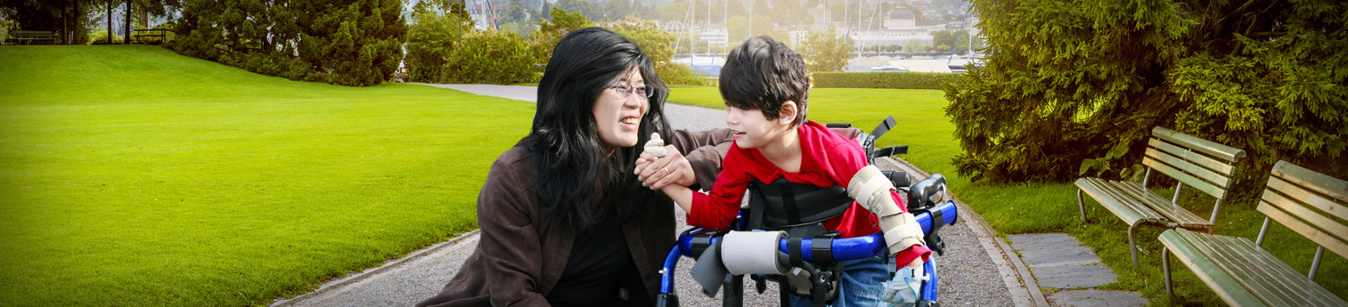 A woman kneeling next to her son who needs a walker because of a physical disability.