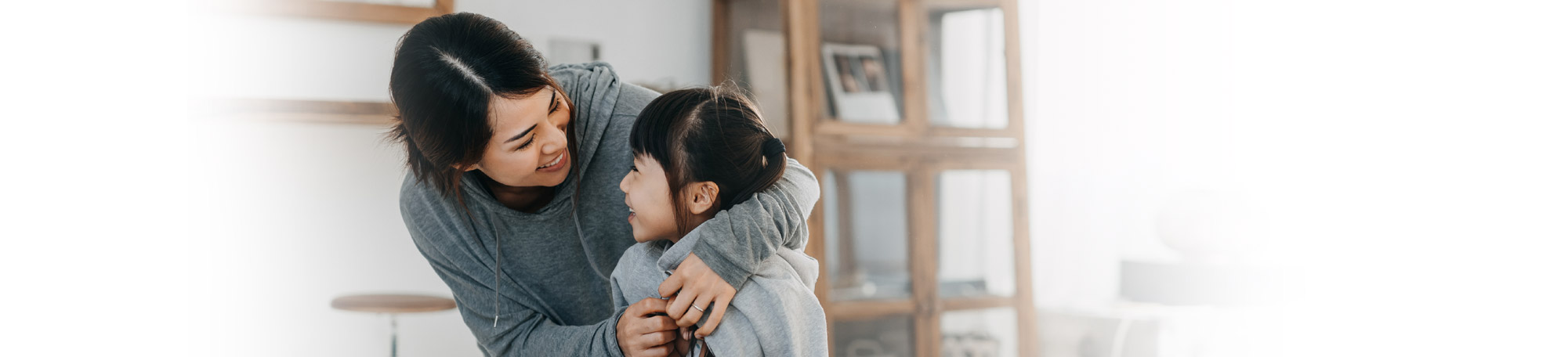 An Asian mother smiles and comforts her smiling child.