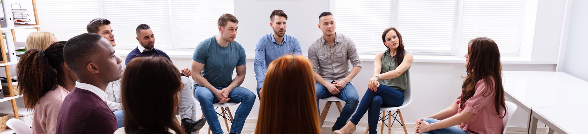 A diverse group of men and women sitting together in a circle for a group counselling session.