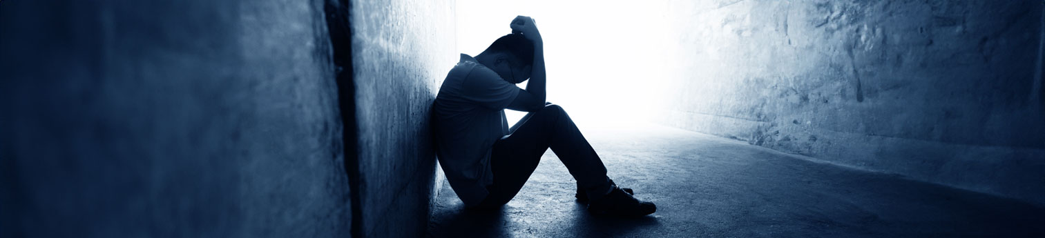 A man sitting alone on the floor in an empty room. His head is in his hands showing he feels alone.
