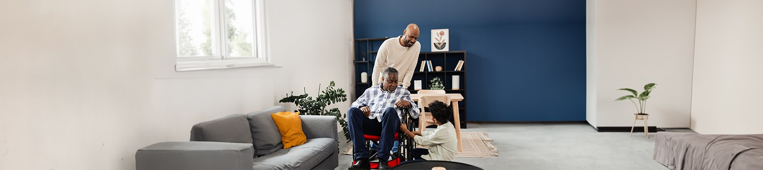 A black boy and his father taking care of his grandfather in a wheelchair, inside the grandfather's home.