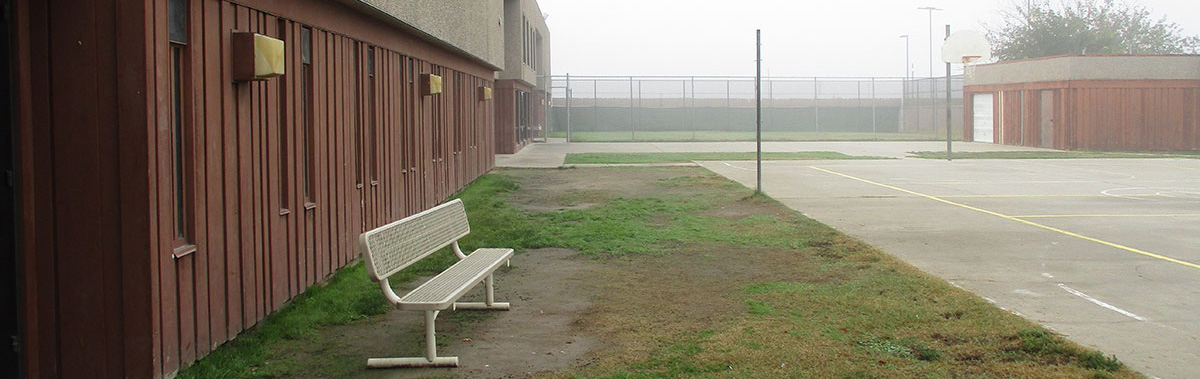 The exterior of the detention center showing a empty bench in the outside courtyard