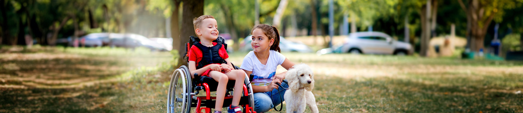 A young smiling boy with a disability and his sister are taking their adorable poodle out on a walk.