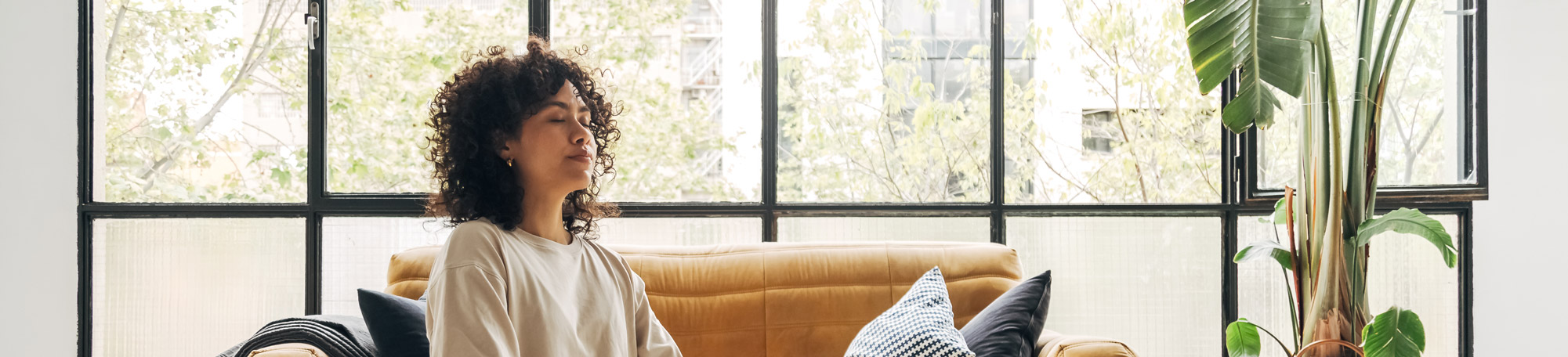 A mixed raced woman practicing breathing exercises in her peacefully looking living room filled with bright calming light.