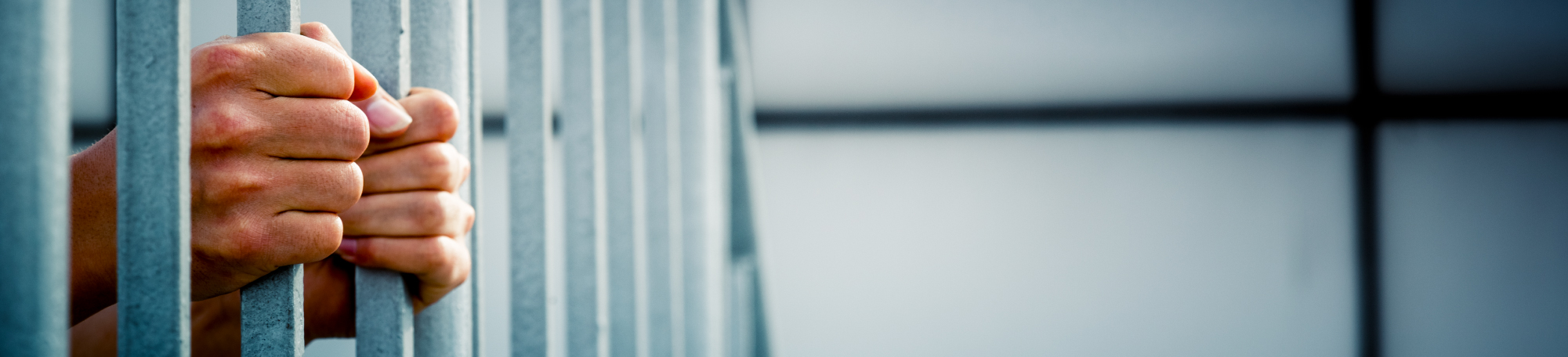 An image of the hands of a prisoner gripping their cell doors.