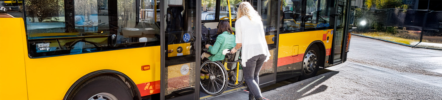 Women with physical disabilities in wheelchair, aided by an assistant to climb on a public bus