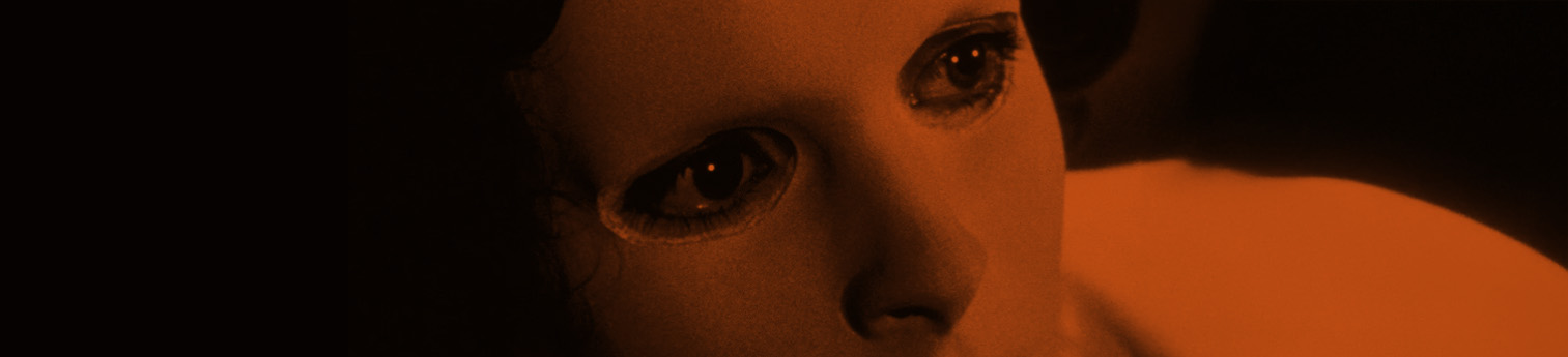 Close-up of a womans face covered bb a plain white face mask. The image has a orange tint.