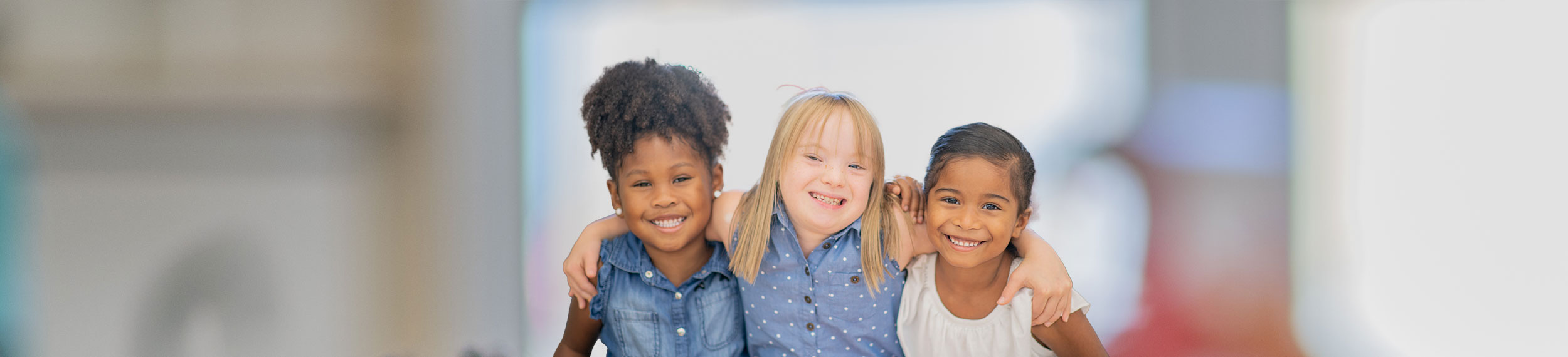 A photo of three young girls hugging each other. They all have a disability.