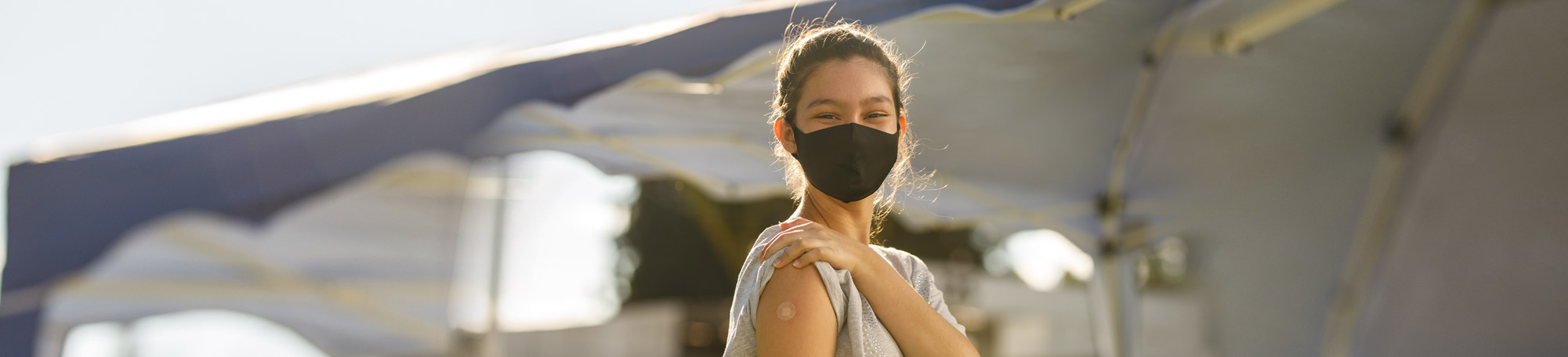 Photo of a young woman at a vaccine clinic showing a band-aid on her arm. She got vaccinated.