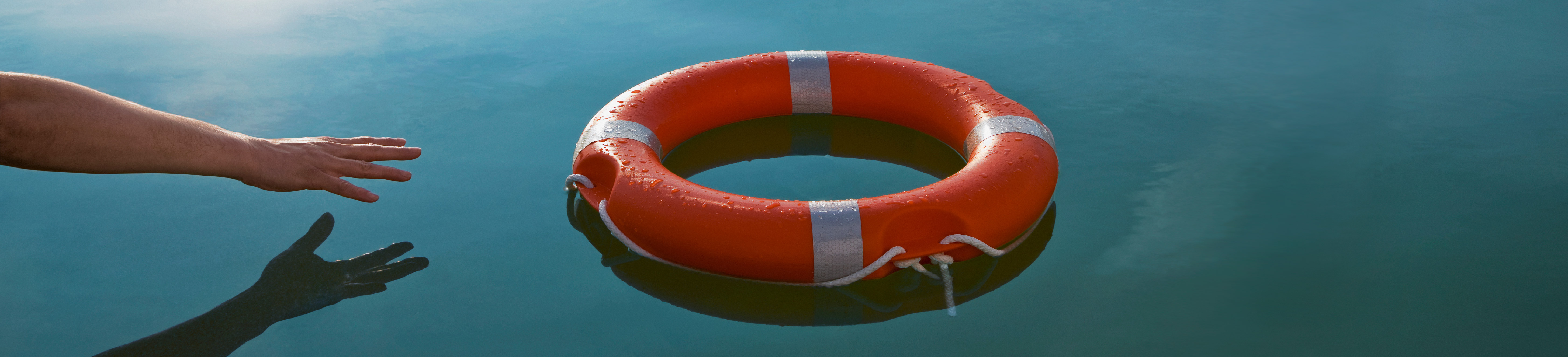 A mans arm reaching out toward a lifeline that is floating on top of a river.