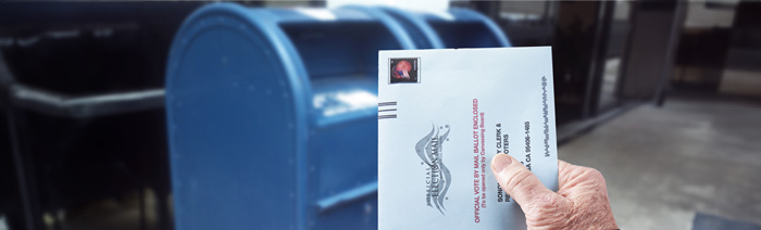 An elderly person placing a vote-by-mail ballot in a mailbox.